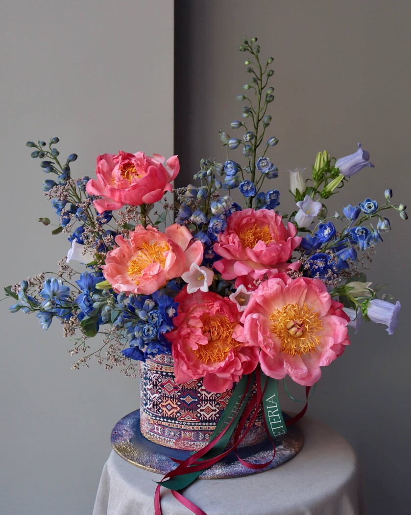 Decorative composition of blue delphiniums, campanulas, and coral peonies