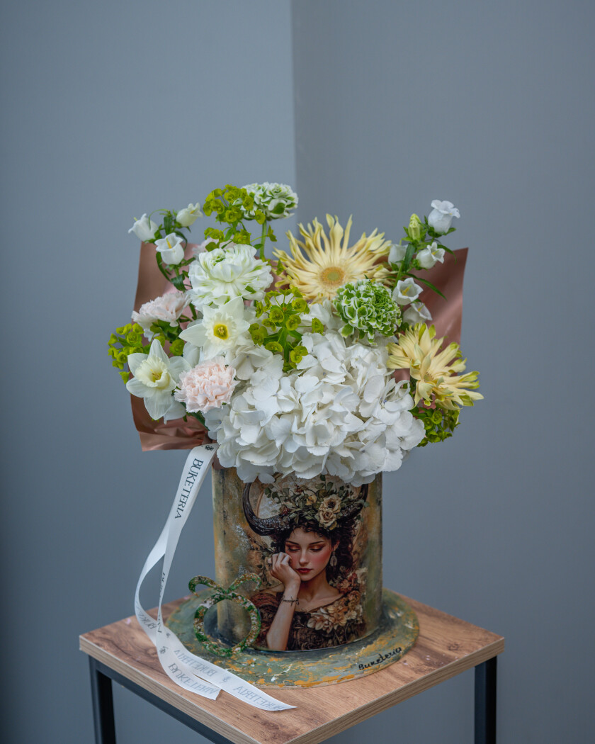 Decorative composition of blush ranunculus and peach carnations in an art box